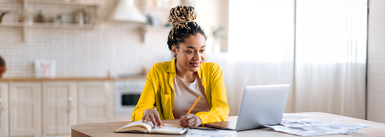 Woman looking at computer and writing in notebook
